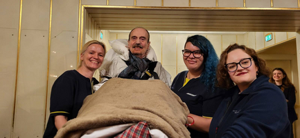 Vier Personen stehen zusammen und helfen einer Person, die auf einer Liege liegt.