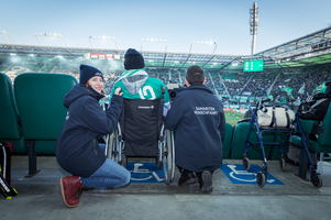 Eine Frau hilft einem Mann im Rollstuhl bei einem Stadionbesuch.