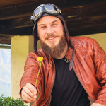 Mann in Lederjacke bietet eine Blume lächelnd an.
