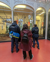Drei Personen betrachten einen Tierkäfig mit Bäumen und Vögeln.