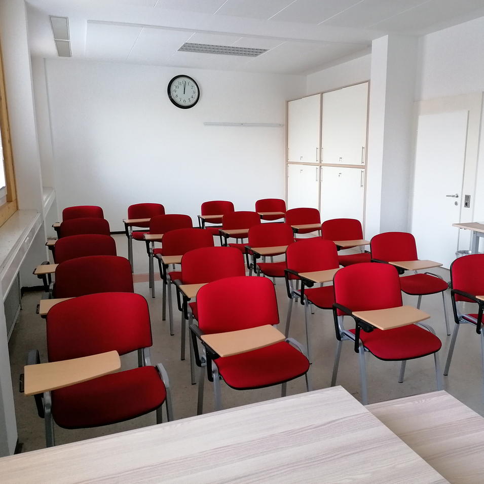 Leerer Klassenraum mit roten Stühlen und einem Wanduhren.