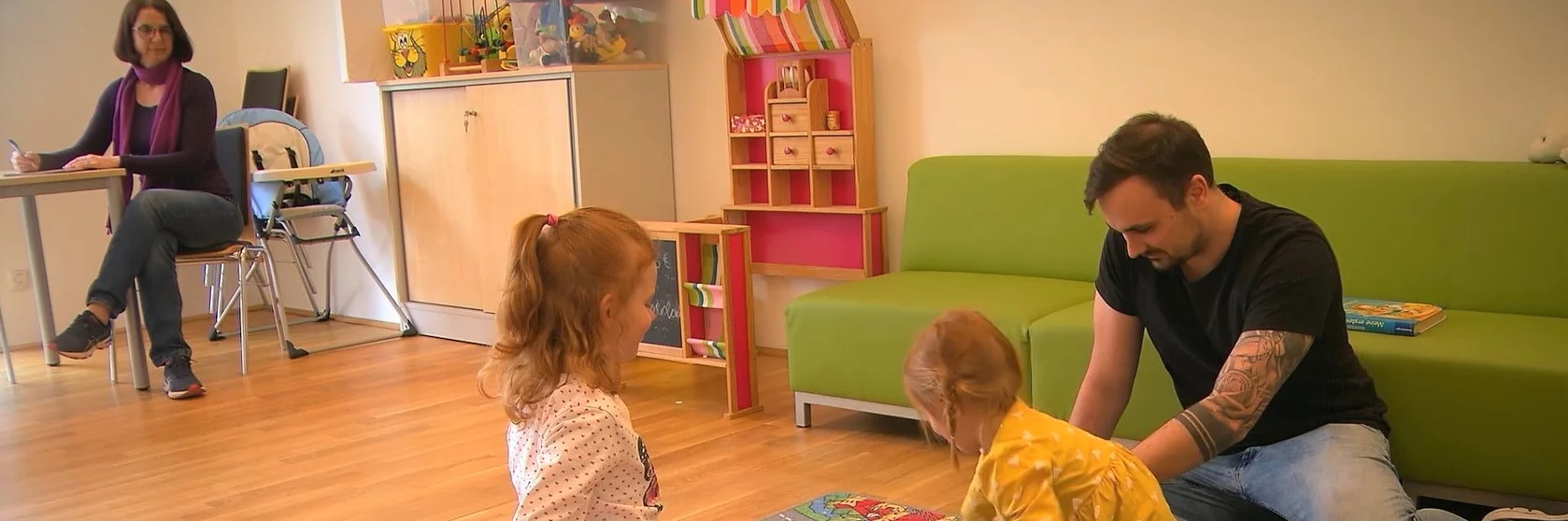 Ein Erwachsener spielt mit zwei Kindern in einem freundlichen Raum.