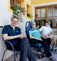 Drei Männer sitzen entspannt auf einer Terrasse und genießen die Sonne.