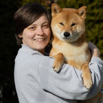 Eine Person umarmt einen Shiba Inu und lächelt glücklich.