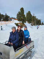 Drei Frauen sitzen auf einem Schlitten in einer verschneiten Winterlandschaft.