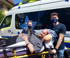 Ältere Dame auf Trage, umgeben von zwei Betreuungspersonen vor einem Krankenwagen.